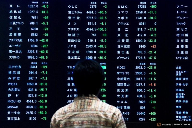A woman stands in front of a display showing market indices at the Tokyo Stock Exchange (TSE). Photo: Reuters.