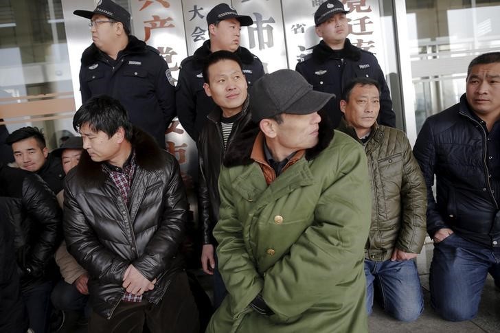 Migrant workers sit in front of policemen as they protest in front of a local government office in Qianan. Photo: Damir Sagolj, Reuters.