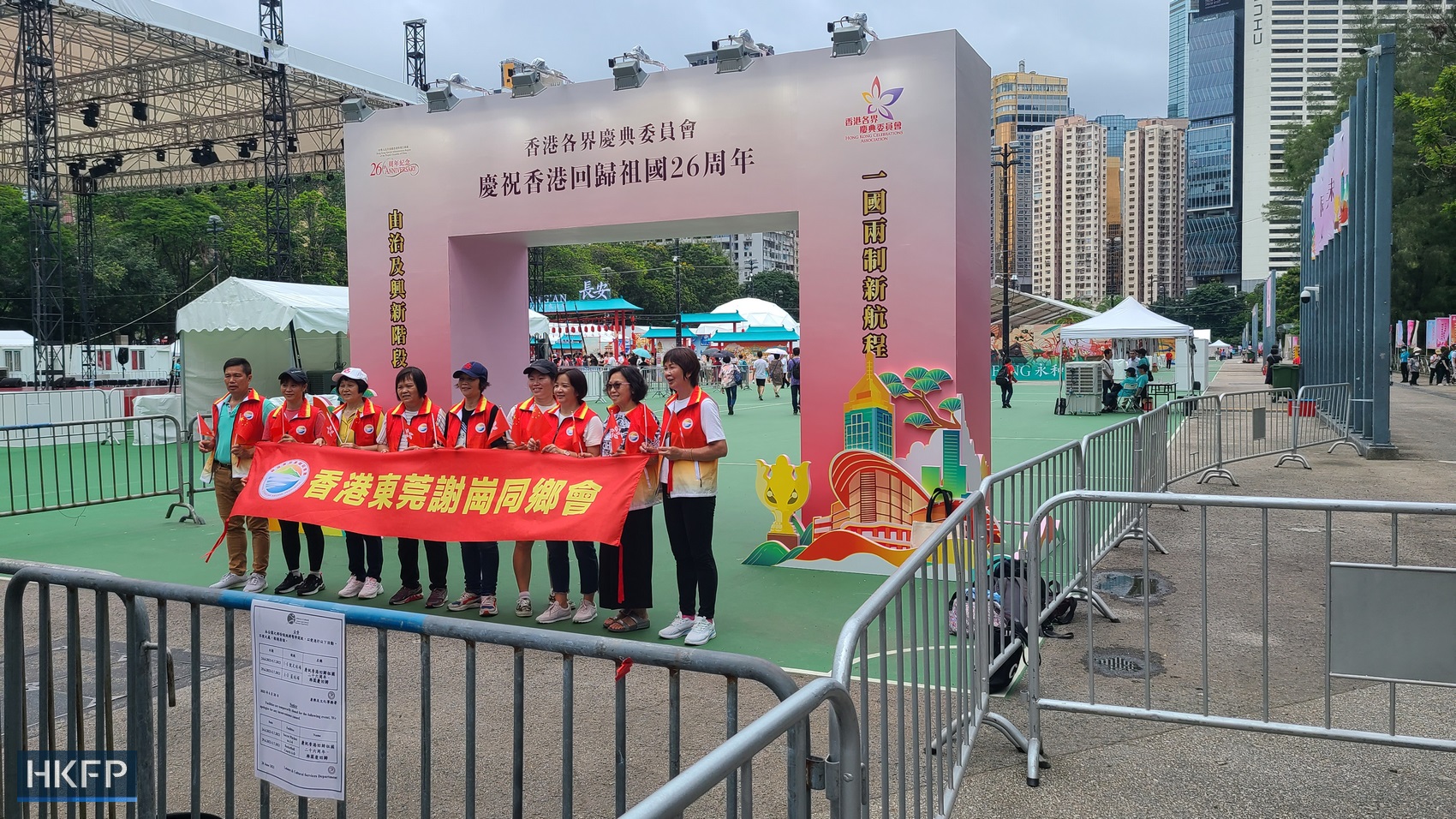 People pose with a banner outside the entrance to an event celebrating the 26th anniversary of Hong Kong's return to Chinese rule at Victoria Park on July 1, 2023. Photo: Irene Chan/HKFP.