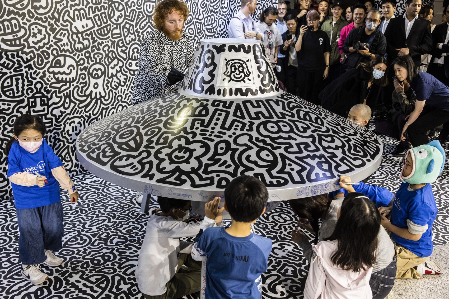 British artist Sam Cox (top), better known as Mr. Doodle, draws on a model spaceship for a live art performance with children from Make-A-Wish Foundation at Central MTR Station in Hong Kong on November 19, 2023. Photo: Isaac Lawrence/AFP.