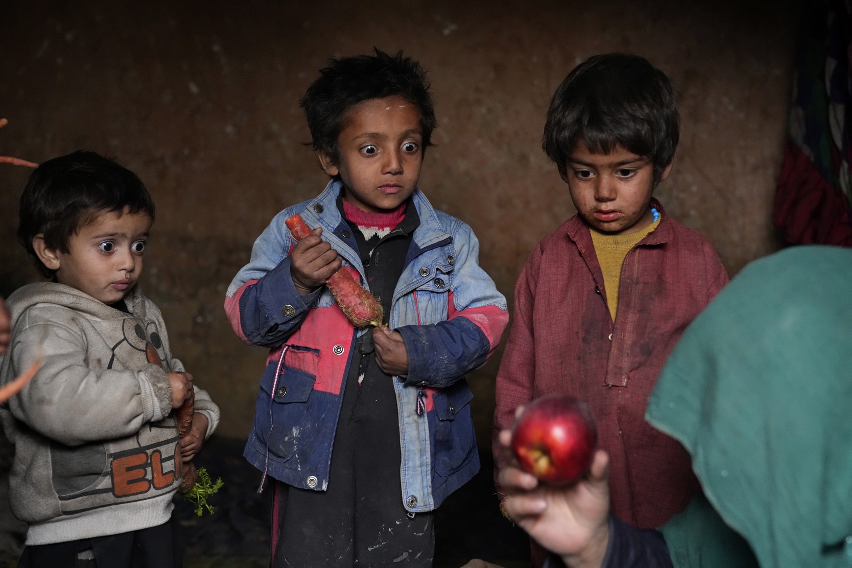 Children stare at an apple that their mother brought home after begging, in a camp for internally displaced people on the outskirts of the Afghan capital. Kabul, Afghanistan, 2 February 2023. 